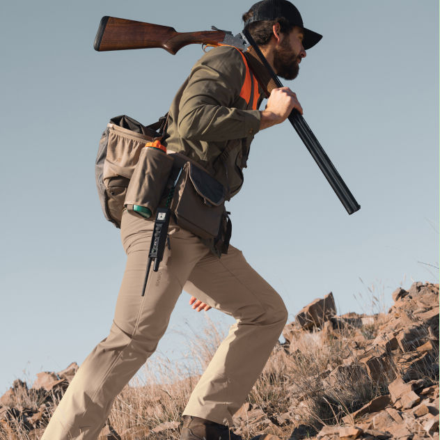 A hunter hikes up a rocky slope.