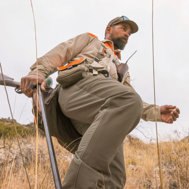 A view from the ground of a hunter picking his way through a brushy field.