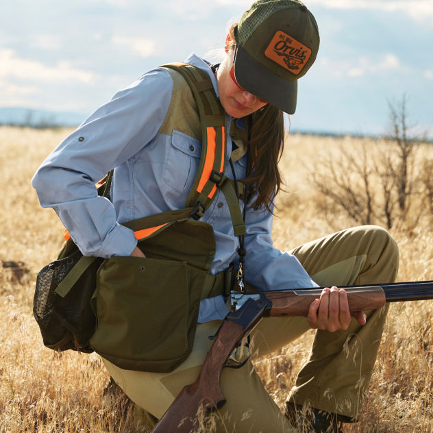 A hunter kneels to looks through her hunting vest pockets.