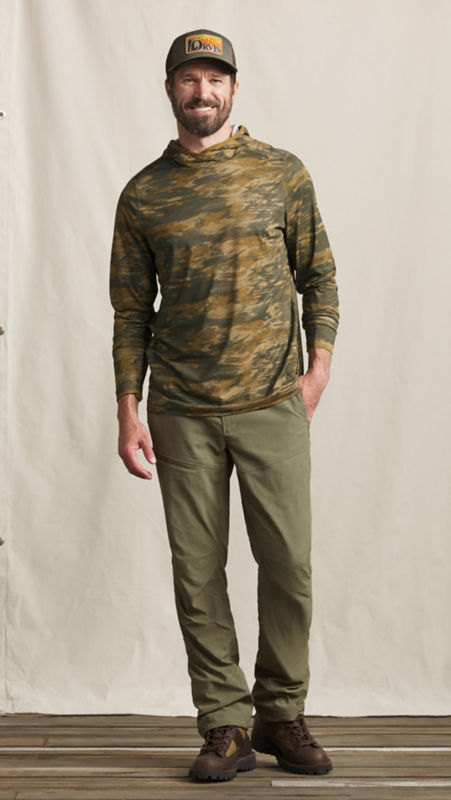 A model wearing an Orvis baseball hat and a hooded performance shirt over olive green pants.
