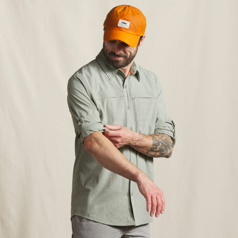 A model adjusts the rolled up sleeves of his sage green button-down.