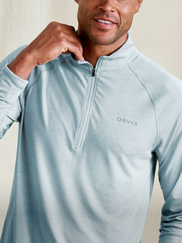 A torso view of a model wearing light blue long-sleeved quarter zip performance shirt with hand on collar.