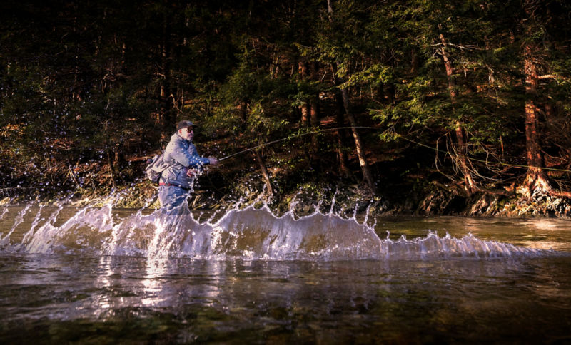 Water splashes up as a fish fights the line in a tea colored river.
