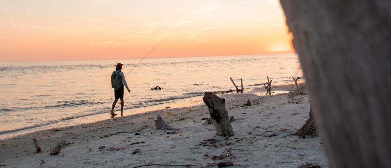 Angler walking on the beach at sunset with fly rod in hand
