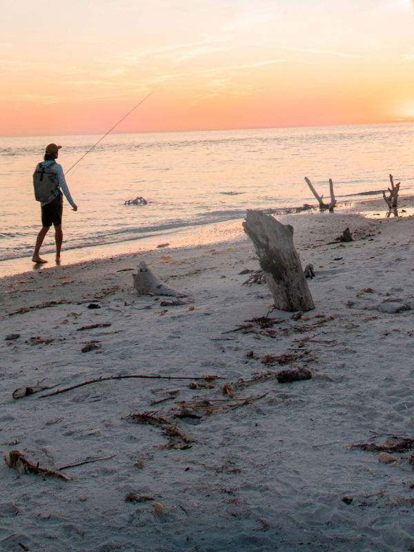 Angler walking on the beach at sunset with fly rod in hand