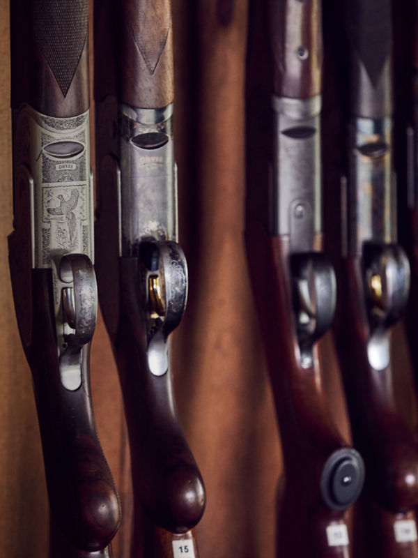 A close-up of several over-under shotguns with wooden stocks displayed in a gun rack.