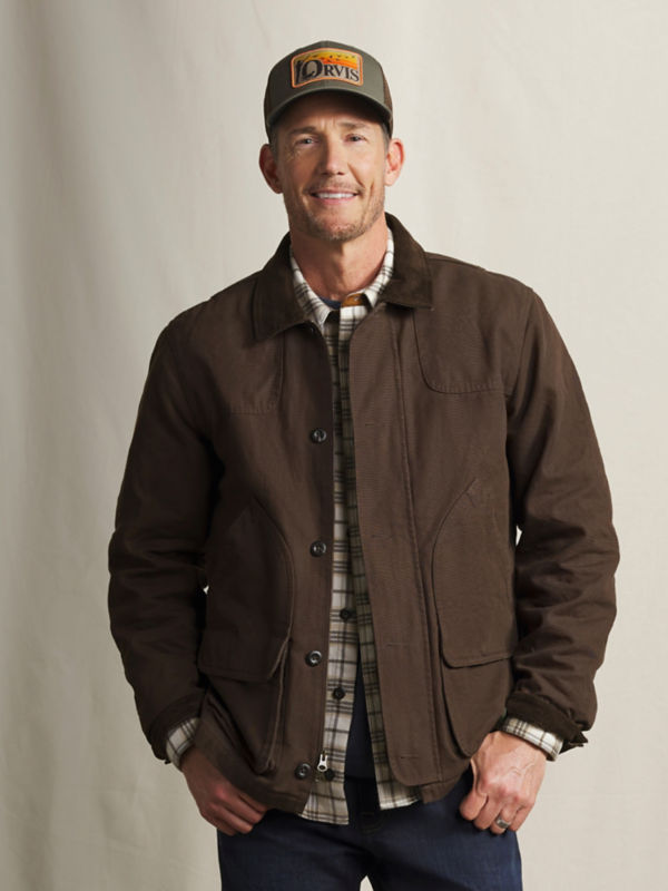 A model wearing a dark brown jacket over a plaid shirt and dark pants.