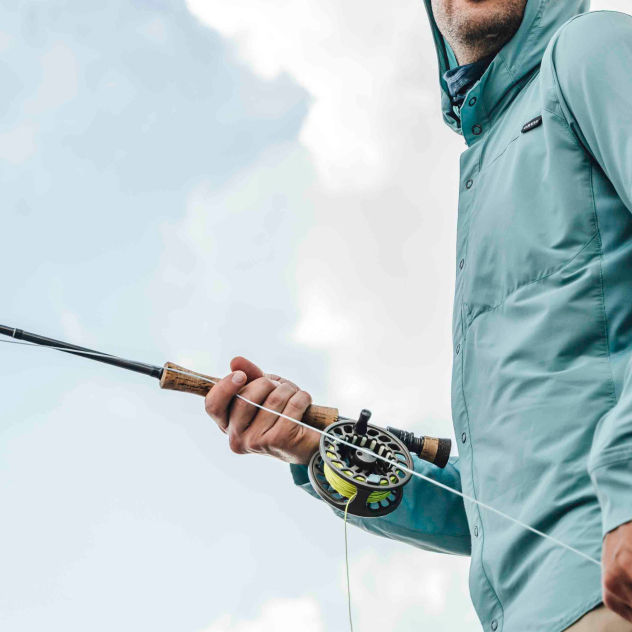 An angler in a hooded sun protective shirt turns while stripping line.