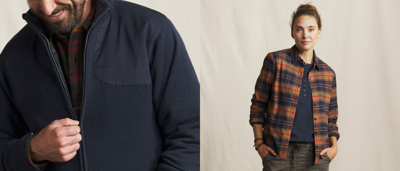 A closeup of a male model wearing a navy blue zip up jacket and a female model wearing a plaid shirt over a navy blue henley.