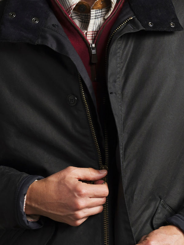 A close-up of a model wearing a Barbour jacket over a flannel shirt and quarter-zip sweater.