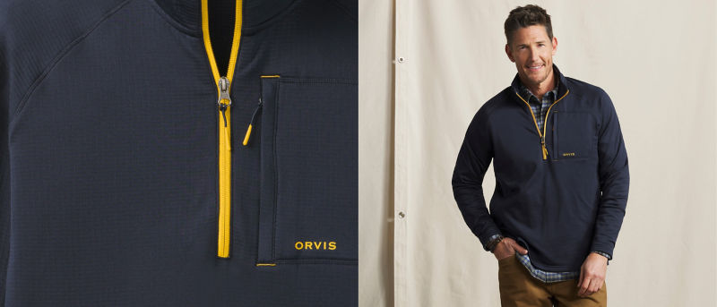 A model wearing a dark blue quarter zip with gold accents over a plaid shirt.