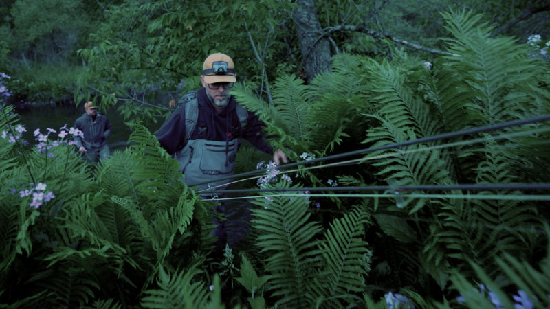 Two men walking through the lush forest holding fishing rods