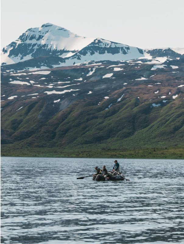 Three anglers rafting in a lake under snowy mountains.