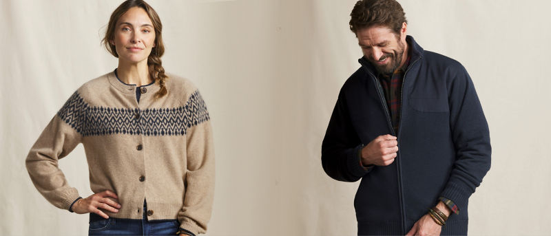 Two models standing against an off-white textured background wearing sweaters.