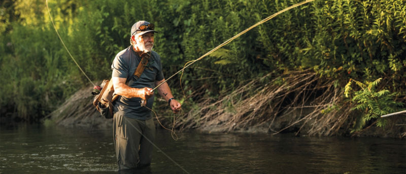Tom Rosenbauer fishes while wading knee-deep in a quiet river.