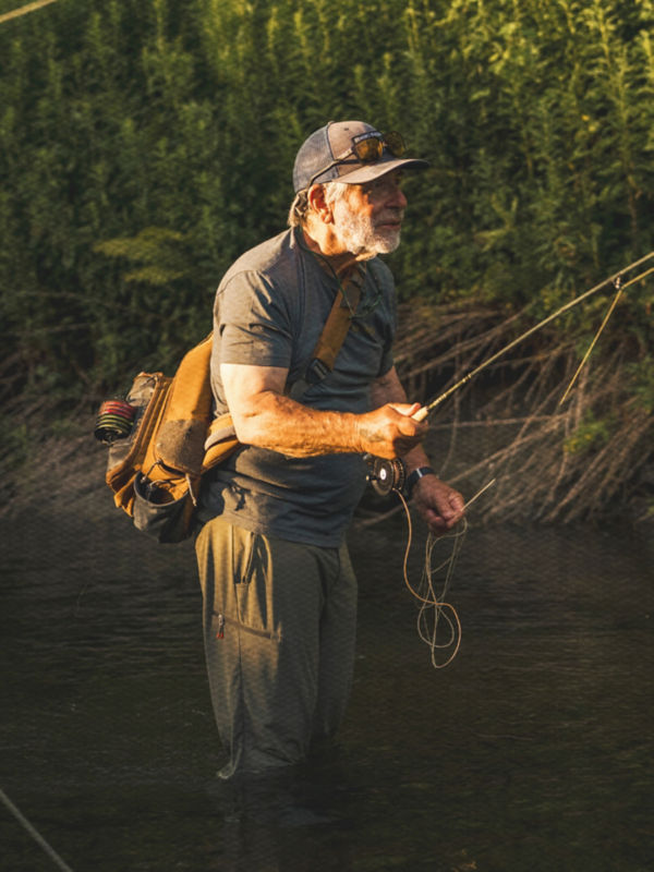 Tom Rosenbauer fly fishing in river with his pack over his shoulder.