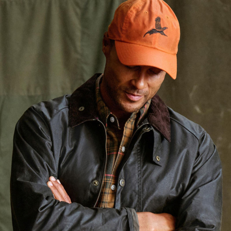 A model wearing an orange ball cap with a pheasant embroidered on the front.