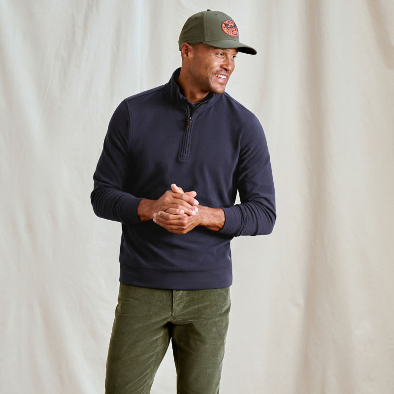 A model wearing a navy sweatshirt over green pants.