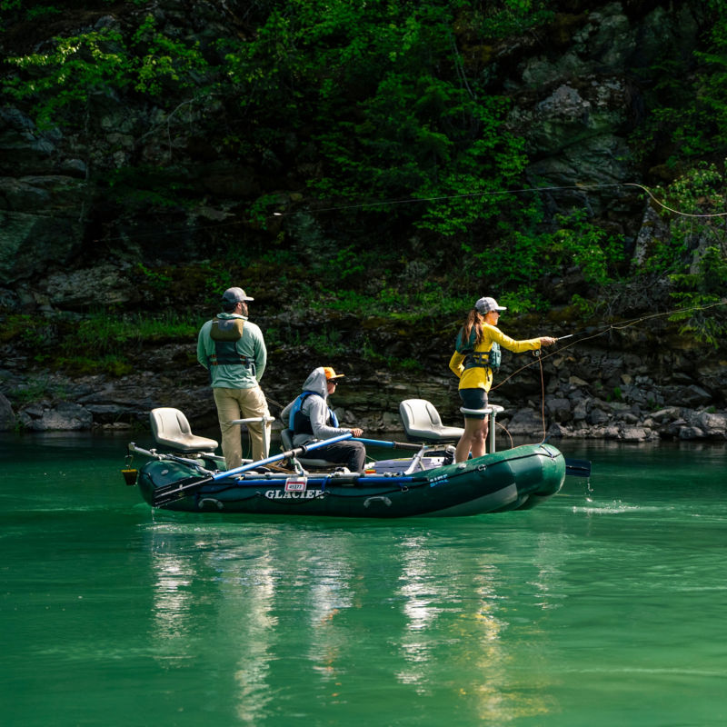A group of anglers in a raft fishing emerald green waters.