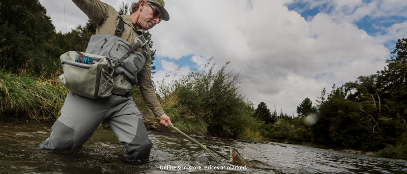 An angler pull his fly rod high while reaching with his net for a fish.