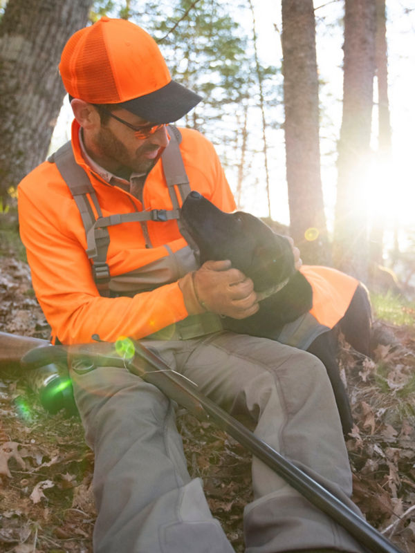 A hunter rests in the woods with his black labrador.