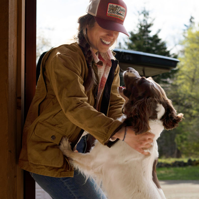 A dog jumps up on a smiling woman leaning against a door jamb.