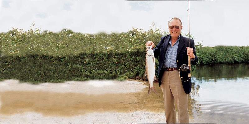 Leigh H Perkins in khakis and blue sports coat holds up a fish he caught.
