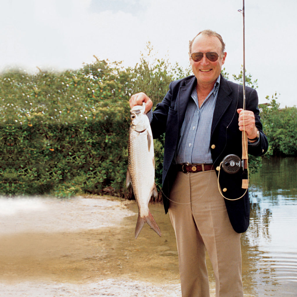 Leigh H Perkins in khakis and blue sports coat holds up a fish he caught.