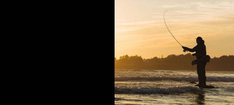 An angler stands among the waves casting at sunrise.