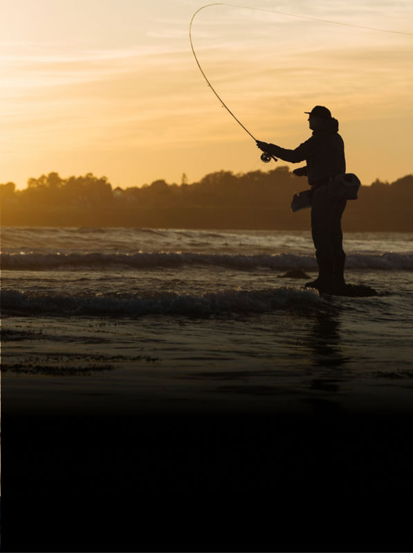 An angler stands among the waves casting at sunrise.