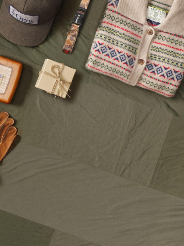 A collection of gifts with such as a ball cap, sweater, and leash laid neatly on an olive green cloth background.