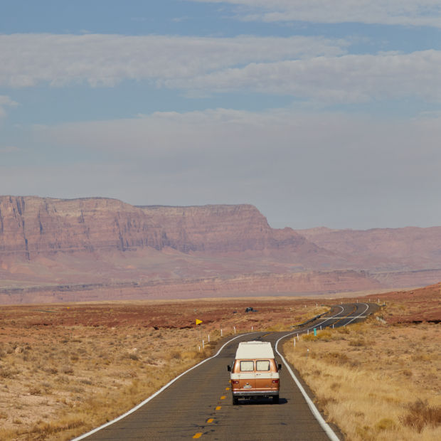 A van trundles down the highway under a giant blue sky, buttes in the background.