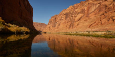 A  river runs smoothly through a red rock western canyon.