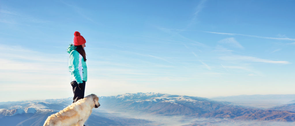 Girl with a golden retriever dog on top of a mountain during winter watching a beautiful landscape