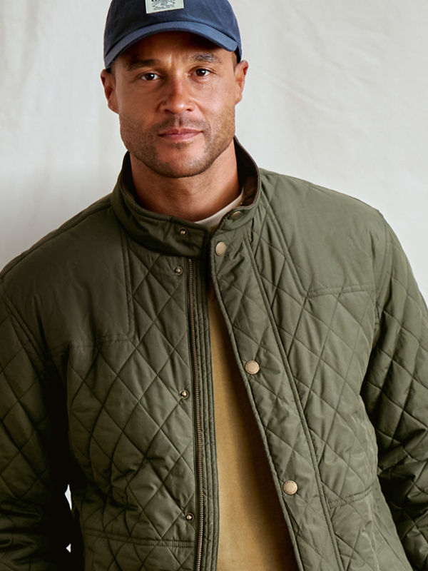 A man wearing a green quilted jacket over a gold tee shirt.