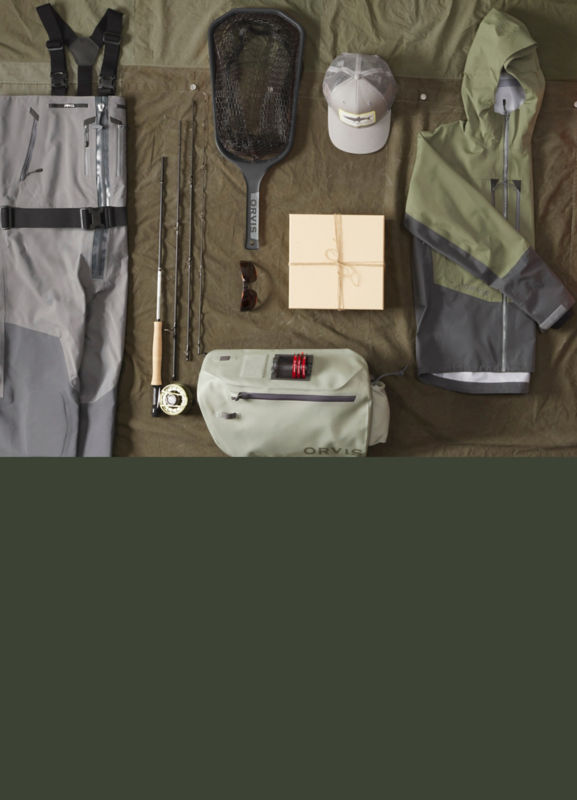 A collection of fishing gear including waders and a fly rod laid neatly on a multi-hued green background.