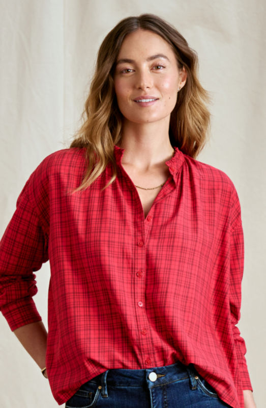 A woman is wearing a red plaid button-down shirt with a gold necklace.