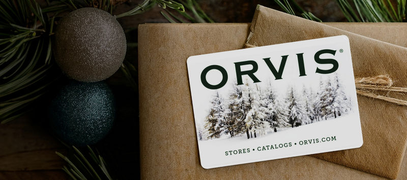 A Orvis holiday gift card on top of presents surrounded by decorations.