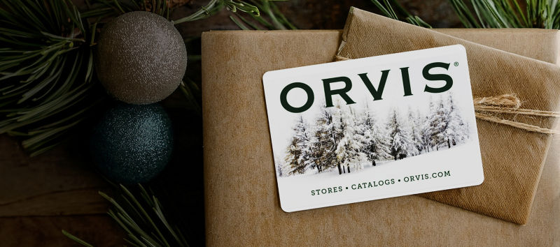An orvis gift card on top of a brown paper wrapped gift box with pine garnishing.