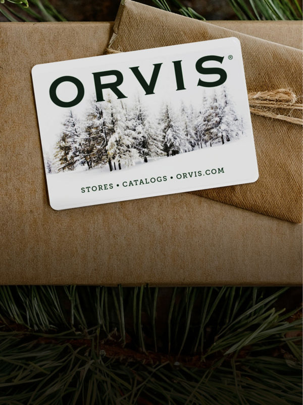 An orvis gift card on top of a brown paper wrapped gift box with pine garnishing.