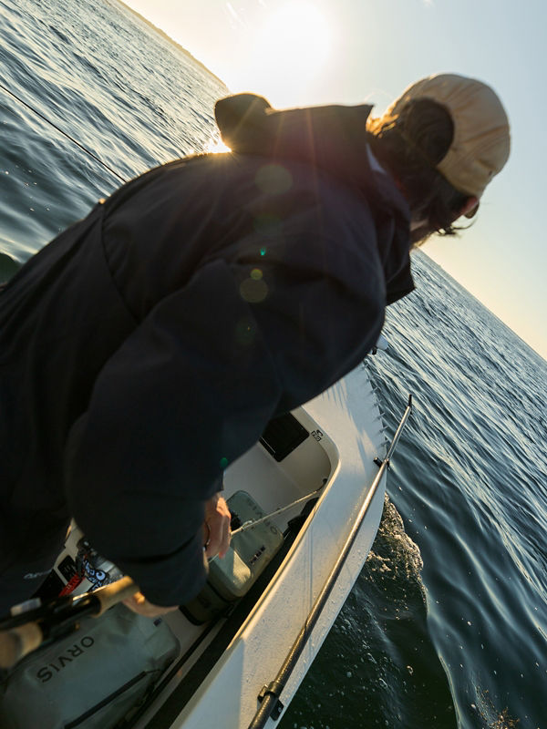 A man wearing a black jacket and tan cap riding on a boat.