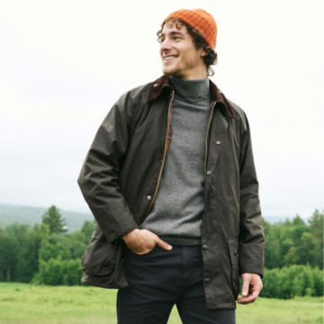Man in Olive Barbour® Classic Beaufort Jacket walks through a grassy field.