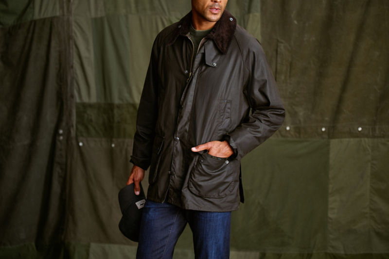 A model in a waxed cotton Barbour&reg; Jacket stands in front of a green canvas backdrop.