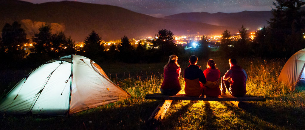 Campers sitting next to a tent overlooking a city at night