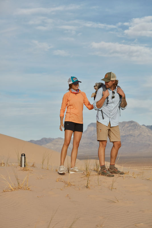 Two hikers in the desert strap up their dog in their backpack.