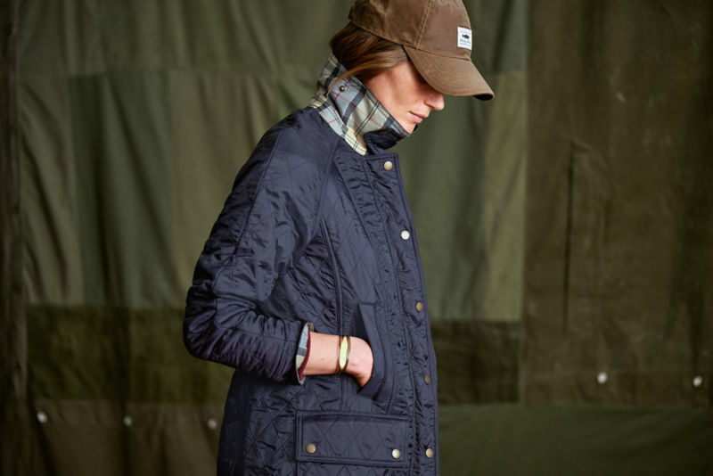 A model wearing a navy waxed cotton Barbour&reg; coat with the collar up showing the plaid underneath.