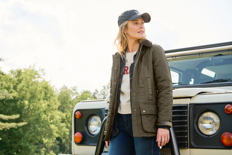 Model wearing olive jacket next to white land rover