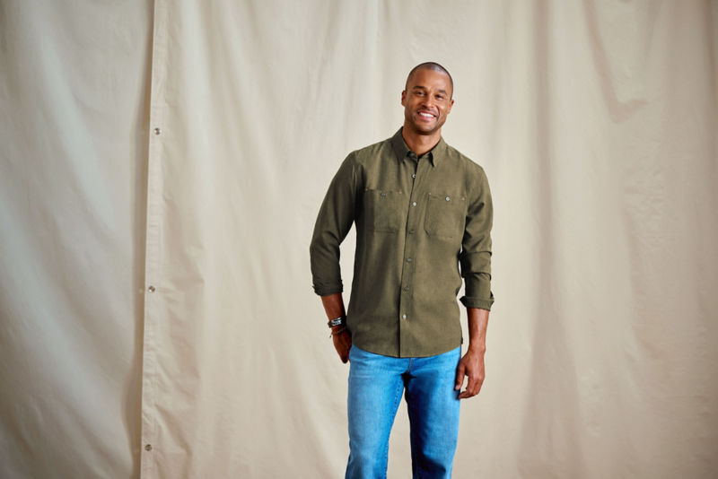 A smiling man stands in front of a canvas backdrop wearing a green button-down.