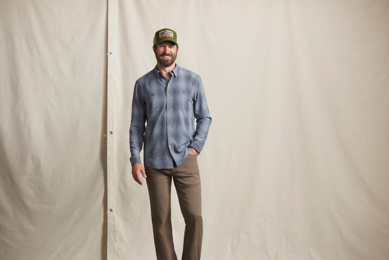 A model wearing a blue long-sleeve button-up shirt, brown pants, and a green trucker hat. 