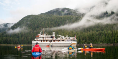 People kayaking in the Alaskan waters near a small cruise ship.